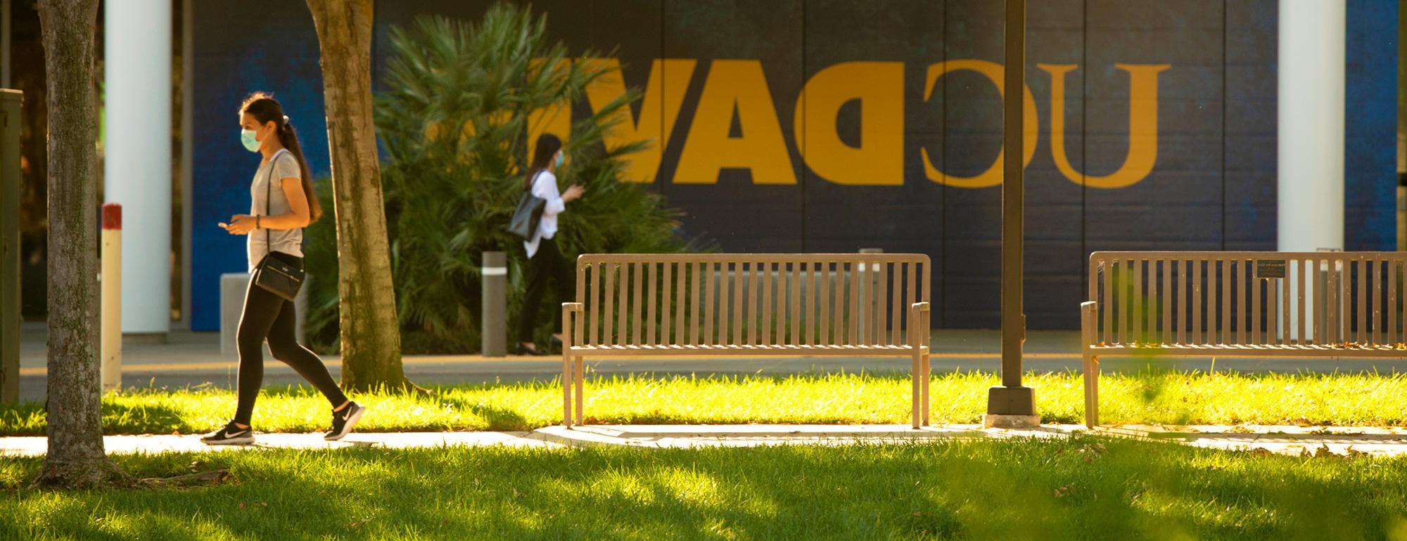一个学生走在校园里. 一个巨大的amjs澳金沙门的标志在建筑的背景墙上.